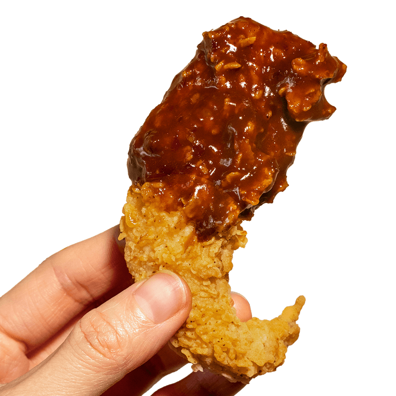 A hand holding a golden crispy fried chicken tender partially dipped in a rich thick spicy soy garlic glaze against a solid black background at Kung Fu Chicken Miami.